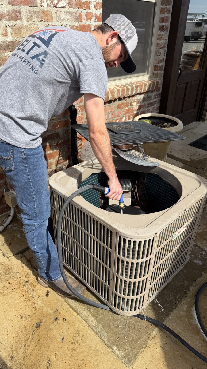 Delta Cooling technician cleaning AC condenser unit in North Louisiana